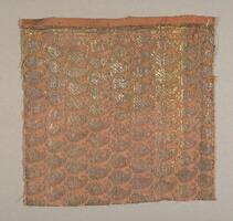 A small fragment of a larger cloth, of unknown function. The base is a plain-weave cotton, now a faded red, and the woven brocade design is of densely-packed, alternating rows of 'boteh' (paisley) patterns.