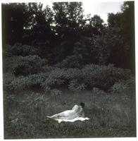 Nude woman with her back turned toward the viewer, reclining in a grassy clearing.