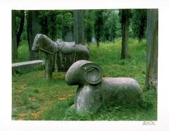 This photograph depicts a forested scene with two large, stone animals occupying the center of the frame.