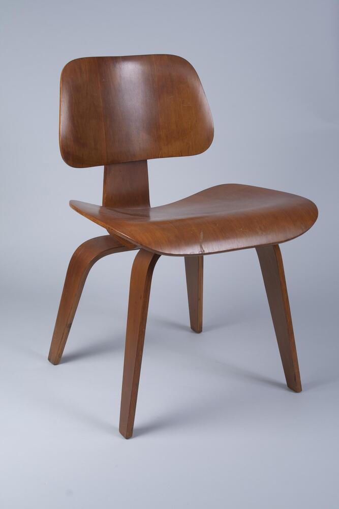 Four-legged plywood side chair consisting of a trapezoidal seat and back connected by a wooden spine.
