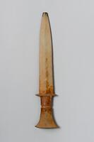 This stone dagger has a handle that is divided into two parts, separated from each other by a thinner band. The upper tier is smaller in length than the lower tier, which flares outward as it approaches the end. The tip of blade is broken off. In profile, the blade thickens in the center.<br />
<br />
Carved from stone, this dagger with a two-tier handle is missing only its tip. The cross section of the blade is rhomboid, while that of the handle is shaped like a convex lens. The dagger is of the later two-tier-handled type (<em>idanbyeongsik</em>), meaning that it probably dates from the end of the early Bronze Age or the beginning of the middle Bronze Age. Max Loehr (1903- 1988) was a German art historian specializing in East Asian art who taught at the University of Michigan from 1951 to 1960 as a professor.<br />
[Korean Collection, University of Michigan Museum of Art (2017) p.32]