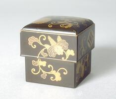 A small square box with lid. Gold lacquered flowers appear on all sides, as well as small crests on one side and on the top of the lid. Part of a bridal trousseau.
