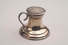 This is a silver-plated sander with a s-shaped handle. It has a circular base that narrows at the top. The lid has a beaded decoration on the rim and small holes. <br />