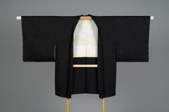 <p>formal black funerary (mofuku) haori with interwoven wave motifs with one kamon (family crest) with an off-white and pale green silk lining with interwoven stylized crane motifs.</p>
