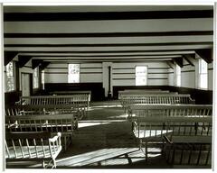 Photograph of the inside of a room with benches and long shadows.