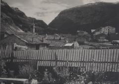 A village situated in a mountain valley. There is a picket fence in the foreground.