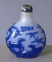 A circular glass snuff bottle with trees and horses on the surface in blue. On top is a lapis lazuli stopper.