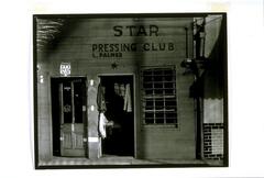 Photograph of the conjoined facades of a barber shop and a laundry, named the "Star Pressing Club."
