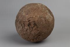This round terracotta sphere has a reddish tint to its rough and cracked exterior.
