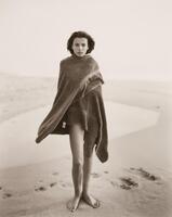 A woman standing on a beach, wrapped in a towel.