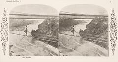 This black and white stereoscopic image features two images of a view of a man standing on one leg, crossing a river on a tightrope next to a bridge.  It is surrounded by the text: Sample Set No. 1; 335 Bloudin.<br />