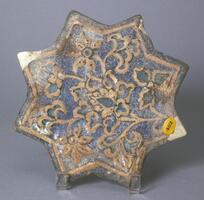 This star-shaped ceramic tile is decorated with floral patterns and shapes. This kind of tile seems to be very popular in the 15th and 16th centuries of the Iranian Islamic world. The relief decoration is moulded and unglazed while the ground is glazed in blues with black underglaze and covered with a clear overglaze. 