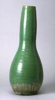 Ceramic vessel with long narrow neck and no foot, lip or rim covered in an iridescent green glaze that covers most of vessel with exposed white-ish clay body at the bottom