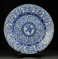 <style type="text/css"><!--td {border: 1px solid #ccc;}br {mso-data-placement:same-cell;}-->
</style>
A blue and white plate centered with a circular panel containing a blossoming lotus encircled by two borders of lappets containing flowering plants, with a shaped rim. There is a studio mark within a double circle on the base.