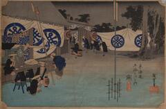 A woodblock print depicting a post town in the Edo period of Japan. There is a wooden structure to the left. It looks like a store, with a list of products hanging on the frame of the door. White flags with a blue circular design hang from the roof to the left and to right near a grouping of trees. Two groups of five men are in front of the structure, five to the left, five towards the center of the image.  A thin vertical stick structure is right of center in the foreground.