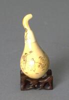 A pear-shaped ivory snuff bottle with a depiction of people and nature. The stopper is the stem of the pear.