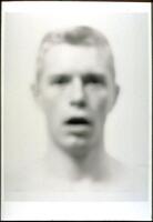 A blurred bust-length portrait of a man's head; he stares straight ahead, his mouth open.