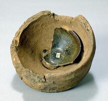 A round, coarse saggar with broken edges, fused to a fragment of a light grey stoneware bowl covered in a dark brown-black glaze with russet and ochre hare's fur mottling (兔毫盏 <em>tuhao zhan</em>). 
