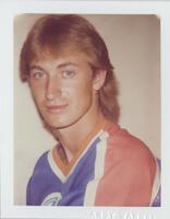 A bust-length portrait of a man. He turns his body toward the left of the frame, his face turned toward the camera. His hair is styled in a mullet, and he wears a sports jersey.