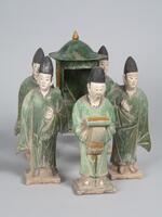 A set of five polychrome glazed male attendants carrying a sedan chair (2001/2.276).  One leads the procession while four carry the chair, all are on a platform. The leader is dressed in long green robes, and is carrying a rectangular box in front of him.  His hands are covered with a tassled scarf, and he is wearing a tall black hat.  His face is painted in polychrome mineral pigments.  The four attendants mirror each other: two on each side, their inside hands holding the sedan, outside hands at their sides, wearing long green robes and tall conical black hats. Their faces are painted with mineral pigments.