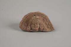 Indian terracotta figure of a woman's head with enormous hair style and hair ornaments.