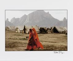 An image of two figures dressed in head-to-toe flowing red garb with their faces obscured. One looks toward the viewer. Tents and a large mountain can be seen in the background.