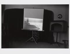 Photograph of a portable tripod screen with projection of airplane in an interior living space. 
