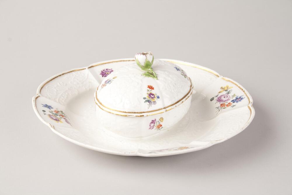 White ceramic dish with attached covered bowl.  Gold leave detail border and flower motifs as decoration.  The handle of the dish cover is a ceramic detailed and painted flower.