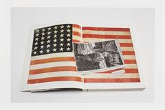 Image of a book lying open to a page featuring an image of the American flag. A newsclipping featuring a photo of a flag manufacturing company lies on the book across the open page.  