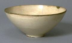 A stoneware conical teabowl with direct rim on straight footring, covered in a cream-colored glaze with craqueleur finish, unglazed rim, and with repair to the body. 