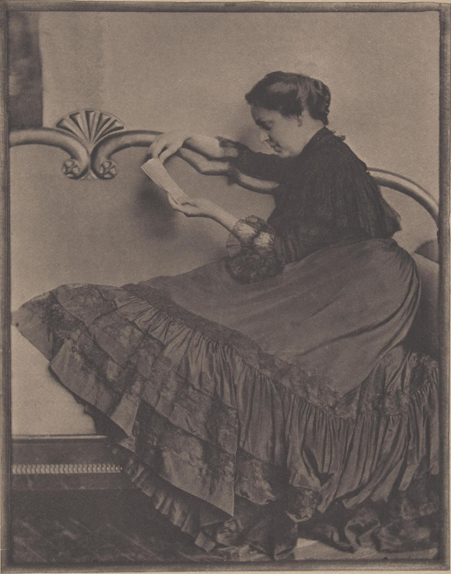 This image depicts a woman in a dress with a large skirt. She lounges on a couch and looks at a book. 