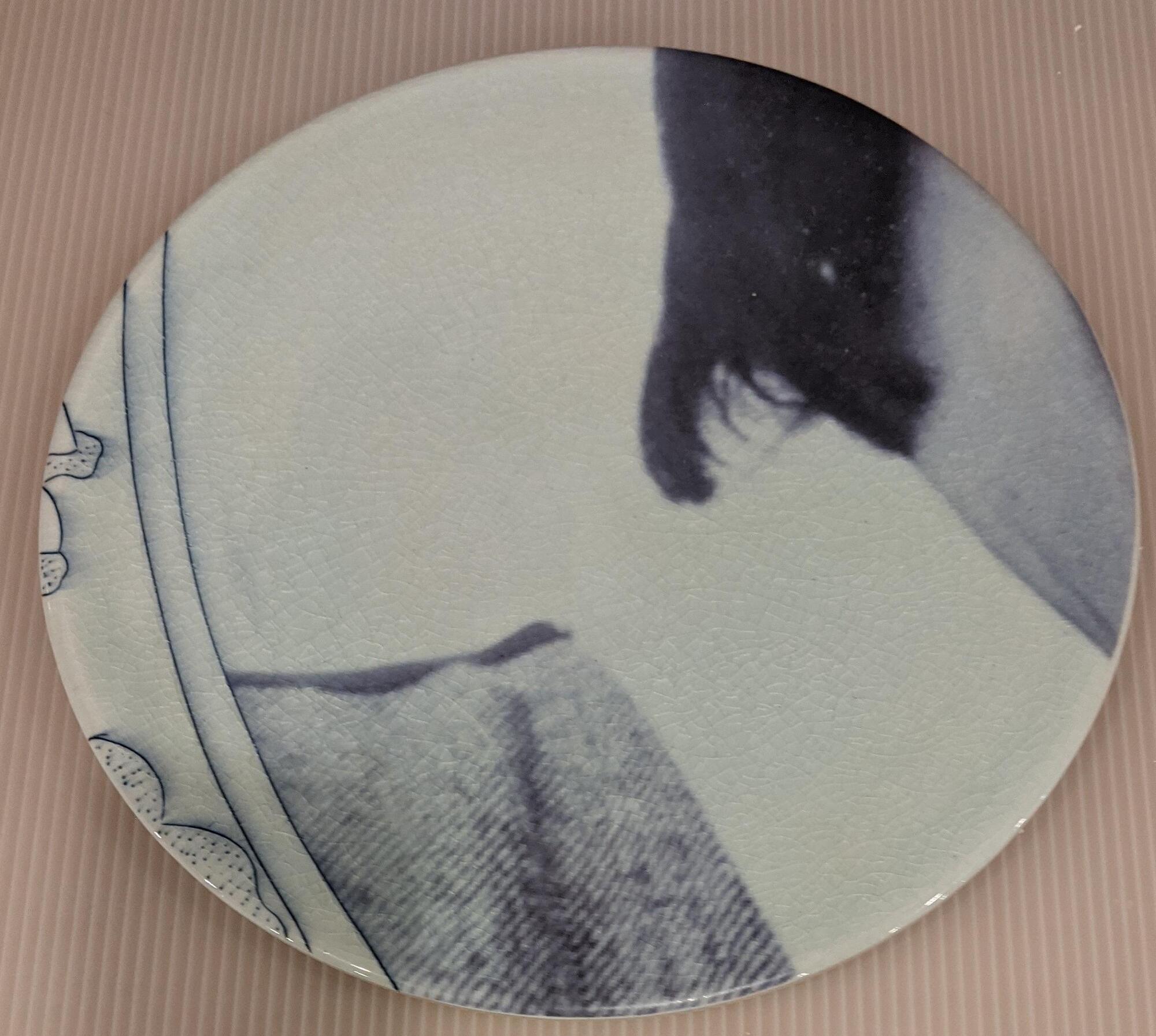 A plate from the center of the piece. A person&#39;s right shoulder and neck are visible. The person is wearing a textured jacket and white shirt. Their dark hair descends to the top of the shirt collar.&nbsp;