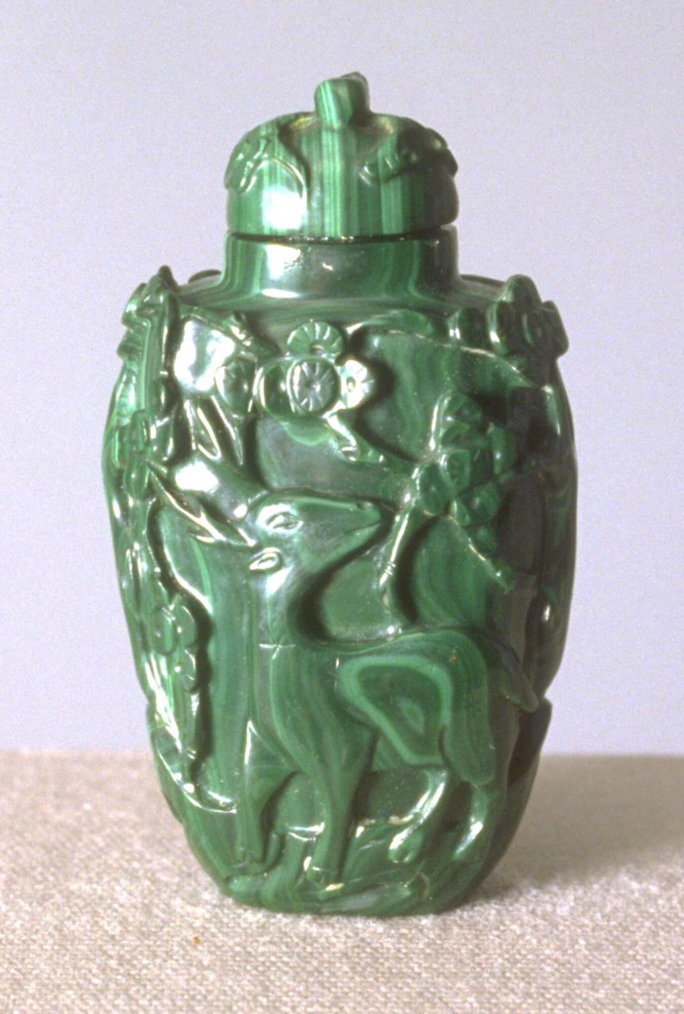 A malachite snuff bottle with carvings of deer and trees. On the top is a malachite stopper.