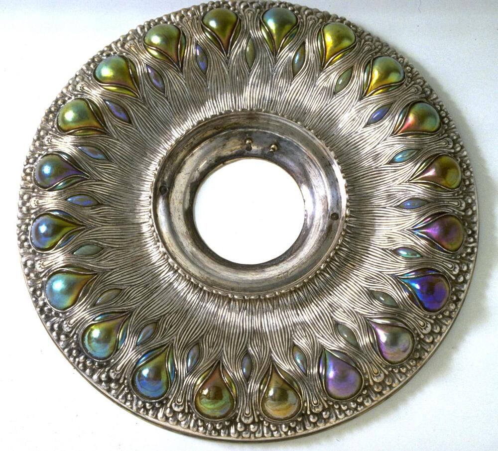 Slivered metal roundel shape with a center opening for a glass globe (suggested). Along the outer perimeter of the roundel are opalescant convex glass shapes evocative of peacock tail feathers.
