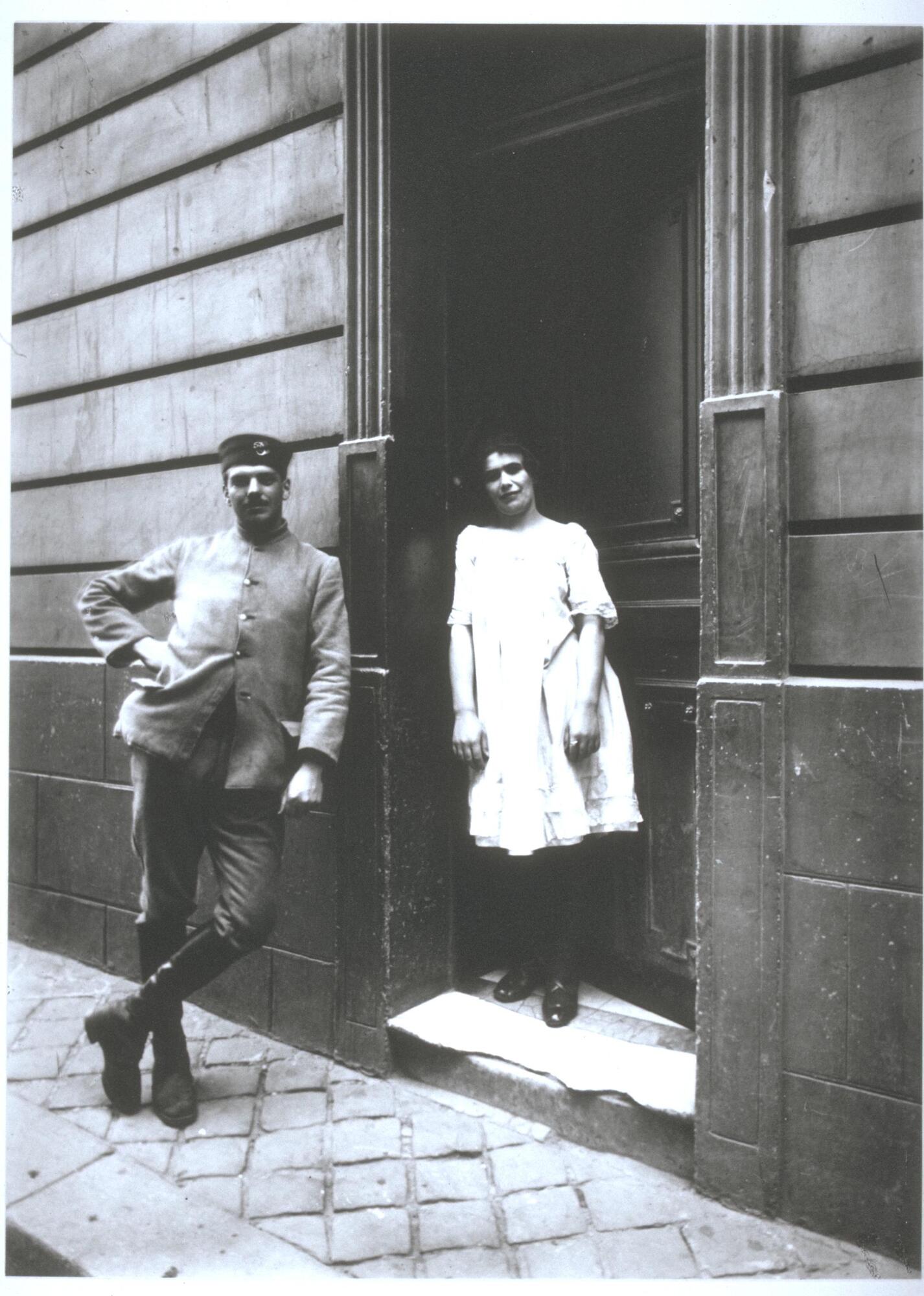 A woman in a doorway and a soldier leaning on the exterior wall next to her.