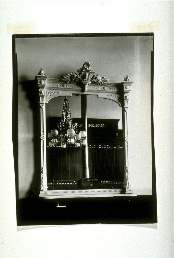 A hall mirror in a hotel lobby reflects an interior adorned with a chanderlier.