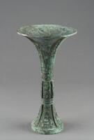 Wine drinking goblet or beaker with a wide, trumpet-shaped mouth, narrow, banded waist, and flaring foot. The slender silhouette of the vessel suggests a date towards the end of the Late Shang period. The body is decorated with Tao-tie mask design, divided by the elaborate raised flanges. An inscription is found inside the flaring foot, presumably the name of the person that the vessel is dedicated or the clan emblem.