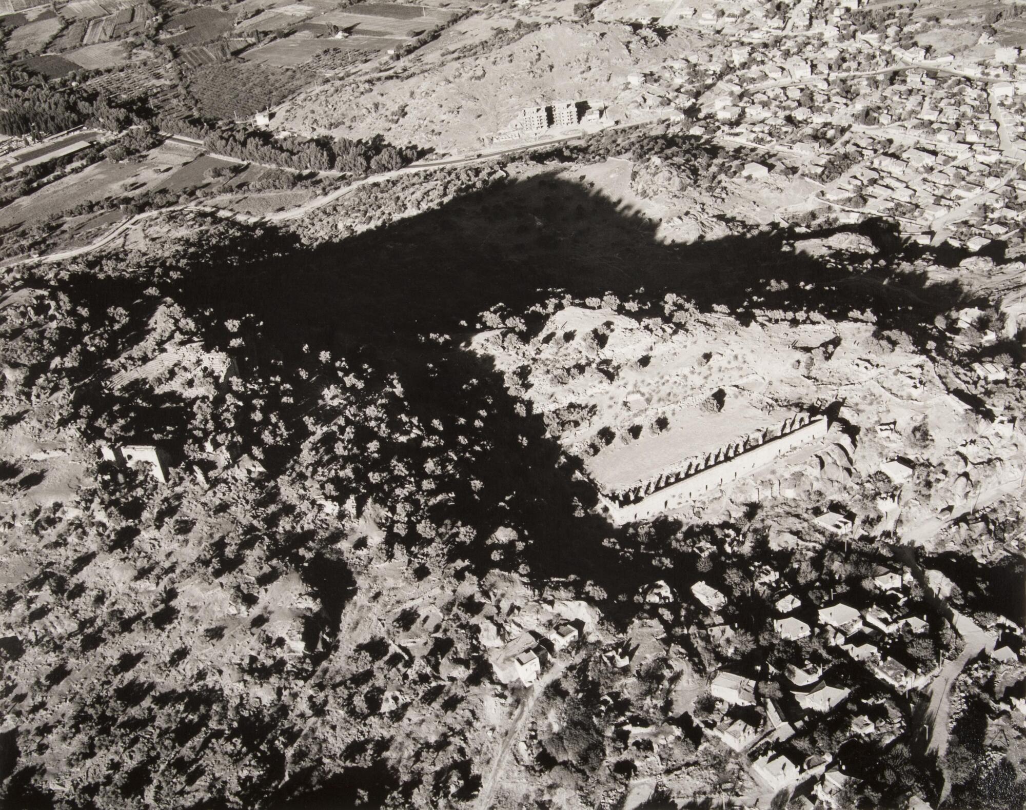 This photograph depicts an aeriel view of ancient ruins situated next to a town on a hillside.