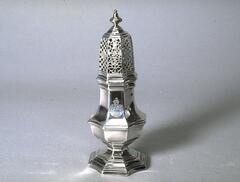 This sugar caster consists of an octagonal body topped by a domed lid. The body stands on a molded, octagonal base with alternating concave sides, a design carried through the rest of the body and the lid. The lid is pierced with geometric and floral patterns that alternate on each facet, and is surmounted by a rounded finial. The tall, slender proportions of the caster are counterbalanced by the horizontal moldings that decorate the base, body and lid. An unidentified coat of arms appears on the body of the caster.