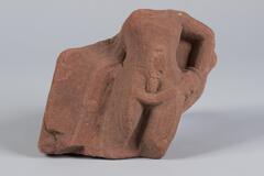 Red stone fragment of a torso and thighs. On the reverse are remnants of white painted letters with only a "6" visible.