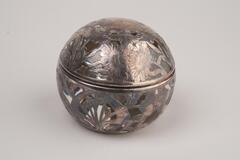 This is a spherical shaped glass inkwell with sterling silver overlay in intricate designs of flowers and plants. The top half of the sphere, which opens horizontally, is the lid.