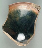 A curved, roughly round-shaped shard with black-brown glaze with russet hare's fur (兔毫盏 <em>tuhao zhan</em>) markings. Broken edges expose a brown ceramic body on a straight footring.