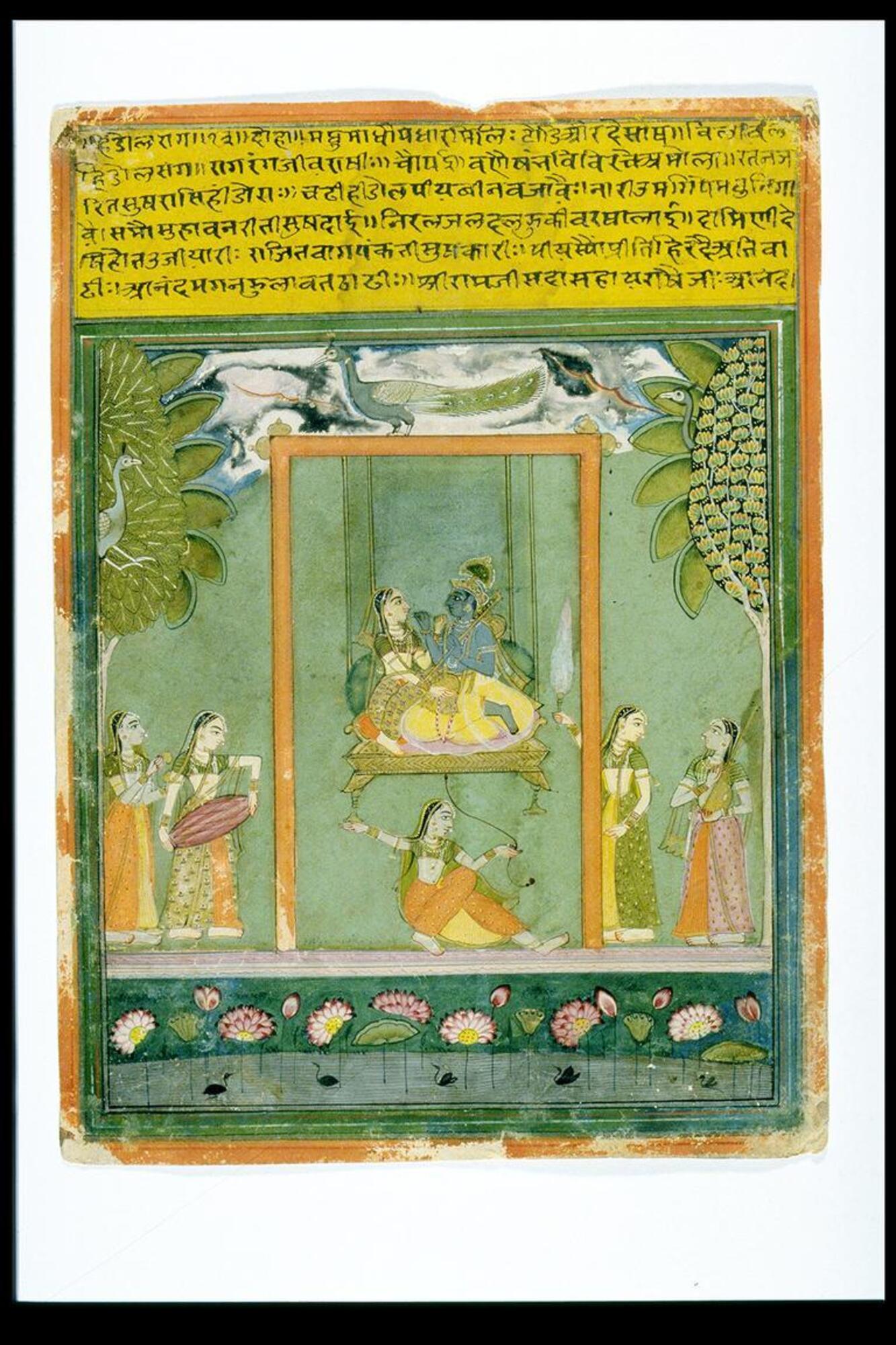 Blue bodied Krishna is shown on the swing with Radha. A peacock stands above the swing frame, and two other peacocks are shown, peering out of the trees shown on the left and right. Five attendants surround the divine couple. One holds the string that, when drawn, will provide the swing its motion; three hold musical instruments, and the fifth a fly whisk. The setting is an open-air garden-like space, with lotuses in the water depicted below the human figures.