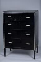 Four-legged black chest of drawers in metal, with contrasting chrome-plated metal in the drawer handles and a thin strip outlining the facade.