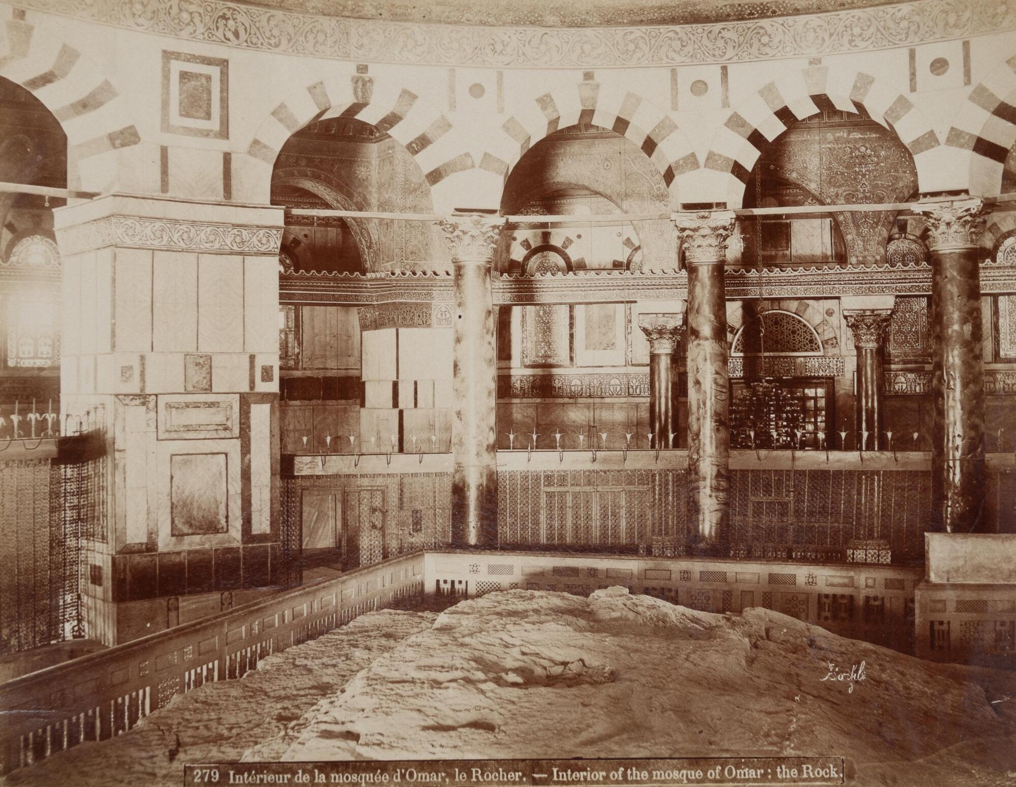 Interior view of a chamber surrounded by a polygonal arcade. The lower register of the photograph shows a large, roughly hewn stone slab.