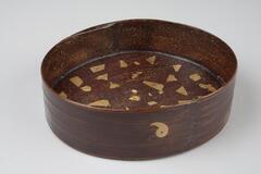Oval wooden lid with one inch lip, circular designs on sides and top. Speckled with gold inside. This is a part of a portable tea set.