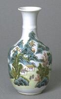 A white vase decorated with a landscape design that includes houses, trees, hills, bushes, and people. The vase has a long, thin neck and an everted rim. The foot of the vase is wide but very short.