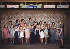 A group of school children singing with a conductor. There is a fabric covered backdrop in a floral pattern.