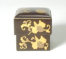 A small, lacquered box with a rounded top. Gold flowers wrap around the sides of the box and there is a small gold crest on the top. Part of a bridal trousseau.