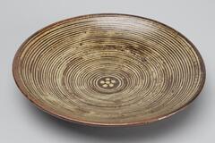Brown round plate with concentric white circles and dots on the interior.&nbsp;